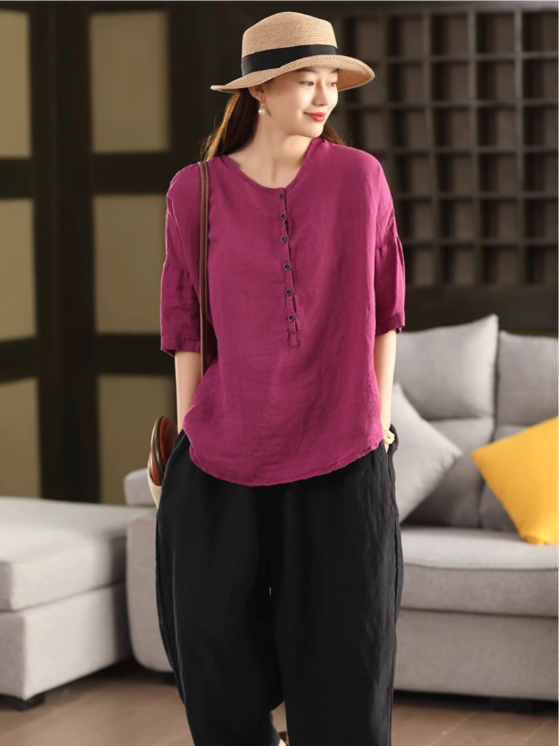 A woman wearing a rose pink solid color shirt top with a classic crew collar and five-point sleeves, paired with black pants.
