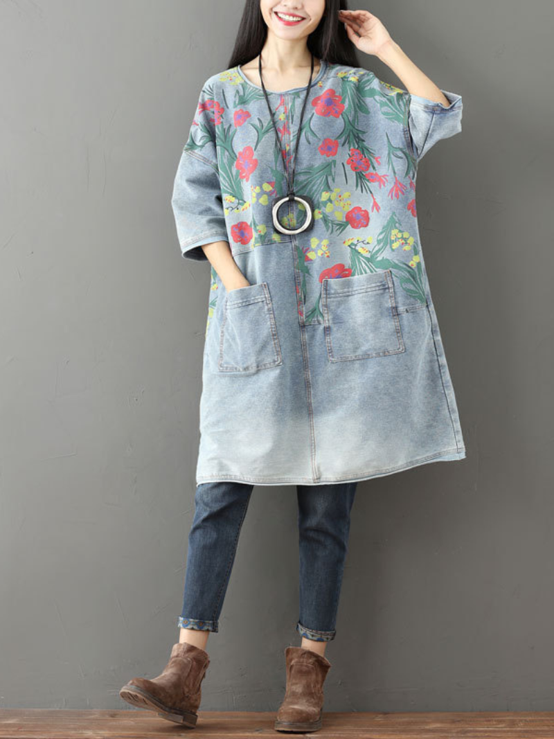 A woman wearing a casual floral midi dress with large pockets, in light blue denim color, paired with jeans and ankle boots.