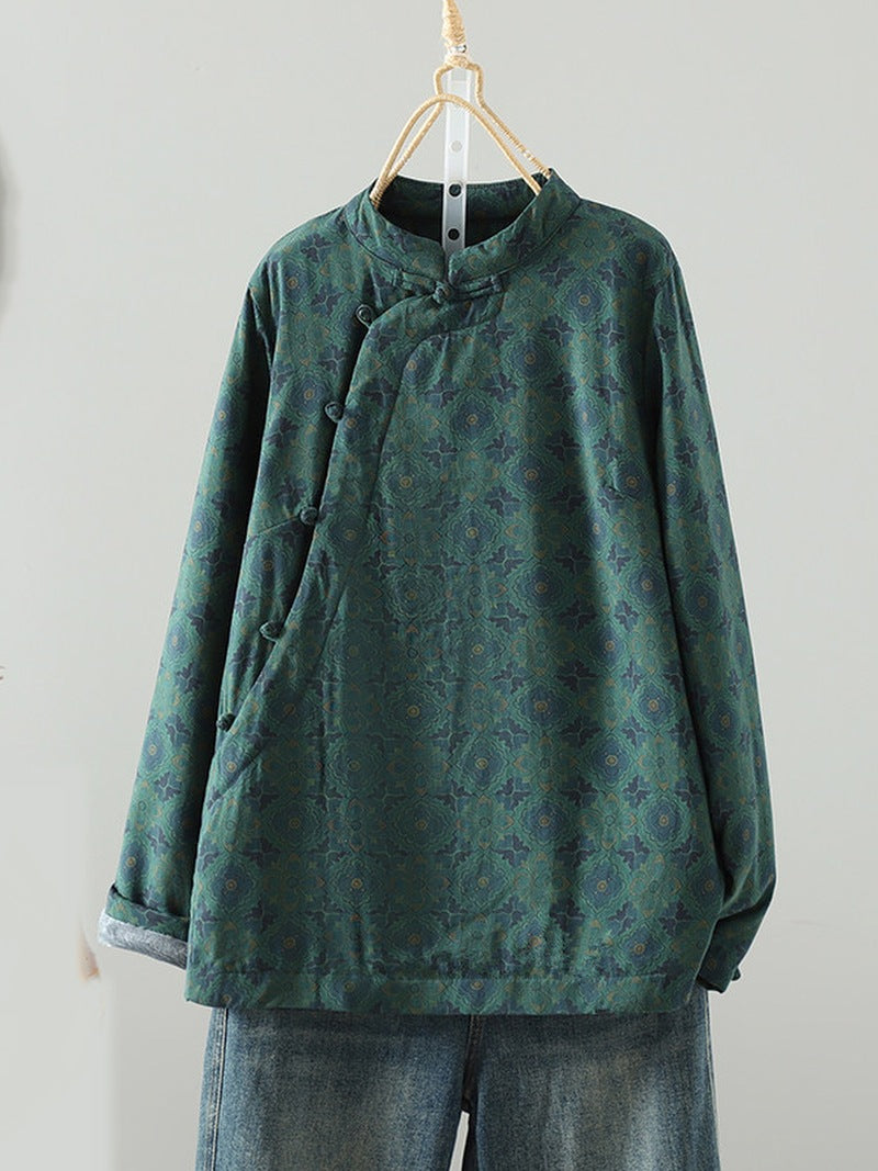 A dark green long-sleeve blouse with a subtle floral jacquard pattern, featuring a mandarin collar and asymmetrical button closure, hanging on a wooden hanger against a plain light gray wall.