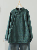 A dark green long-sleeve blouse with a subtle floral jacquard pattern, featuring a mandarin collar and asymmetrical button closure, hanging on a wooden hanger against a plain light gray wall.
