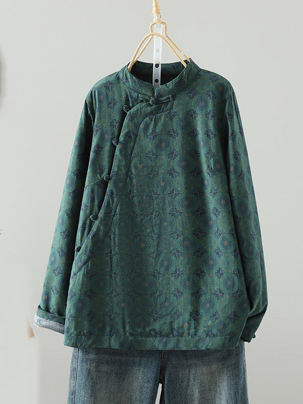 A dark green long-sleeve blouse with a subtle floral jacquard pattern, featuring a mandarin collar and asymmetrical button closure, hanging on a wooden hanger against a plain light gray wall.