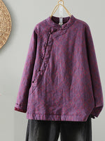 A purple patterned long-sleeve jacket with a mandarin collar and asymmetrical button closure, hanging on a wooden hanger against a light gray wall.